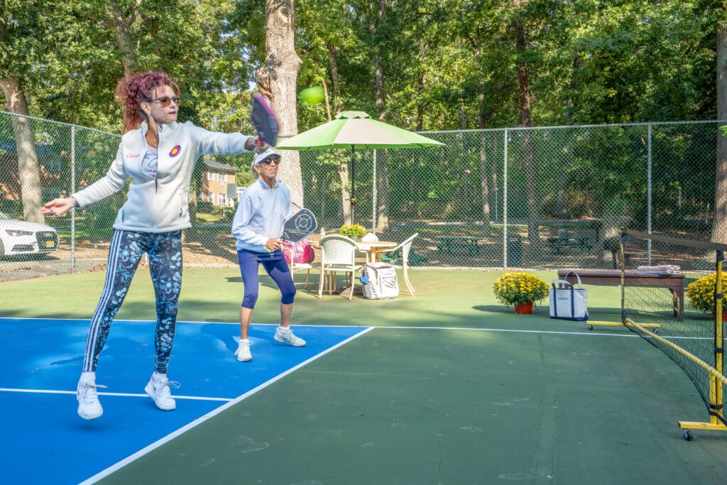 Two women playing tennis on a court in the park.