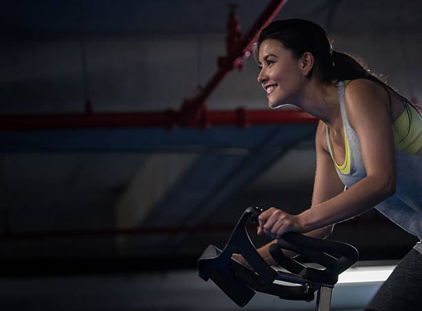 A woman is smiling while riding an exercise bike.